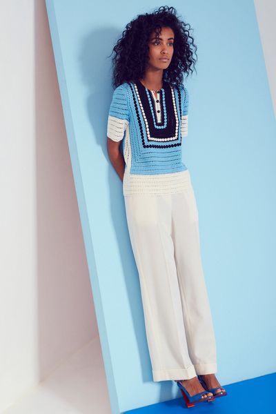 A model wearing white pants and a blue sweater standing in front of a blue background