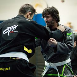 Keanu Reeves grabs partner’s lapel, drilling jiu-jitsu technique.