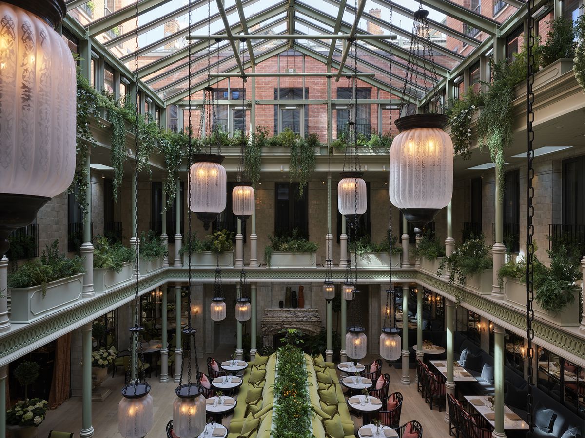  An atrium with a dining area on the first floor, plant-filled balconies, and a glass-pane roof from which lanterns hang at varying heights.