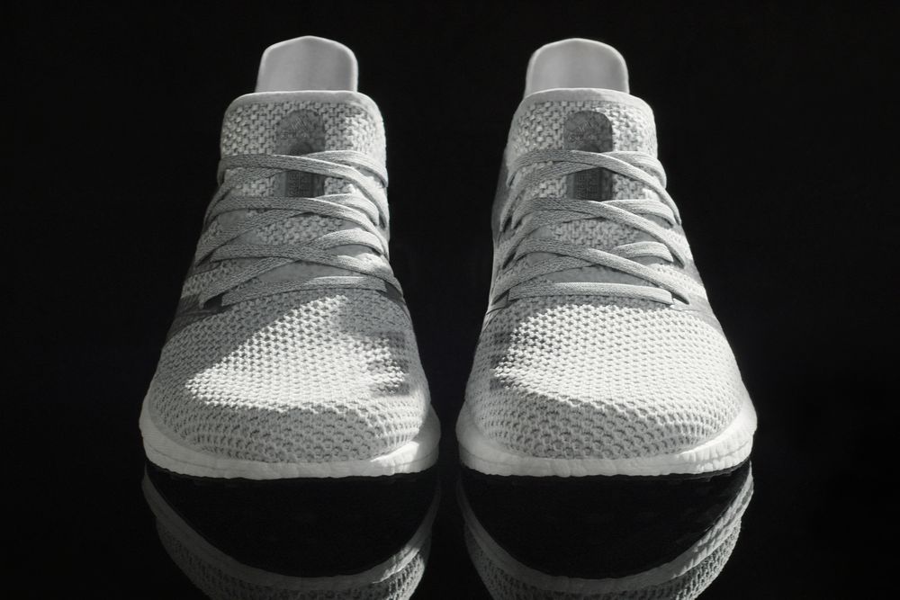 A pair of white and grey sneakers, seen from the front, on a black background. The laces are part of the shoe, you don't have to tie them. They are covered in a sort of mesh. 